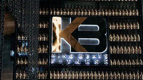 Lit King Beats Fitness logo on a wall of gold bottles